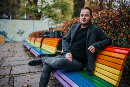 Jon Martin Lrsen sitter på en regnbuefarget benk mens han ser mot kamera. Foto.