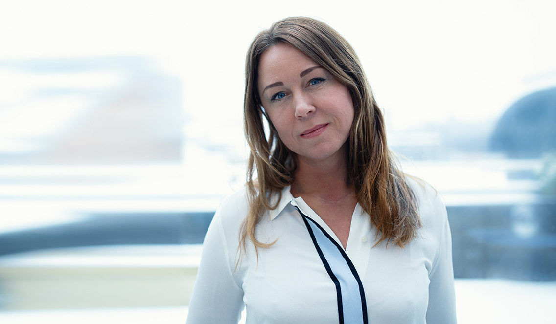 Wenche Witberg står med hodet på skakke foran en glassvegg.