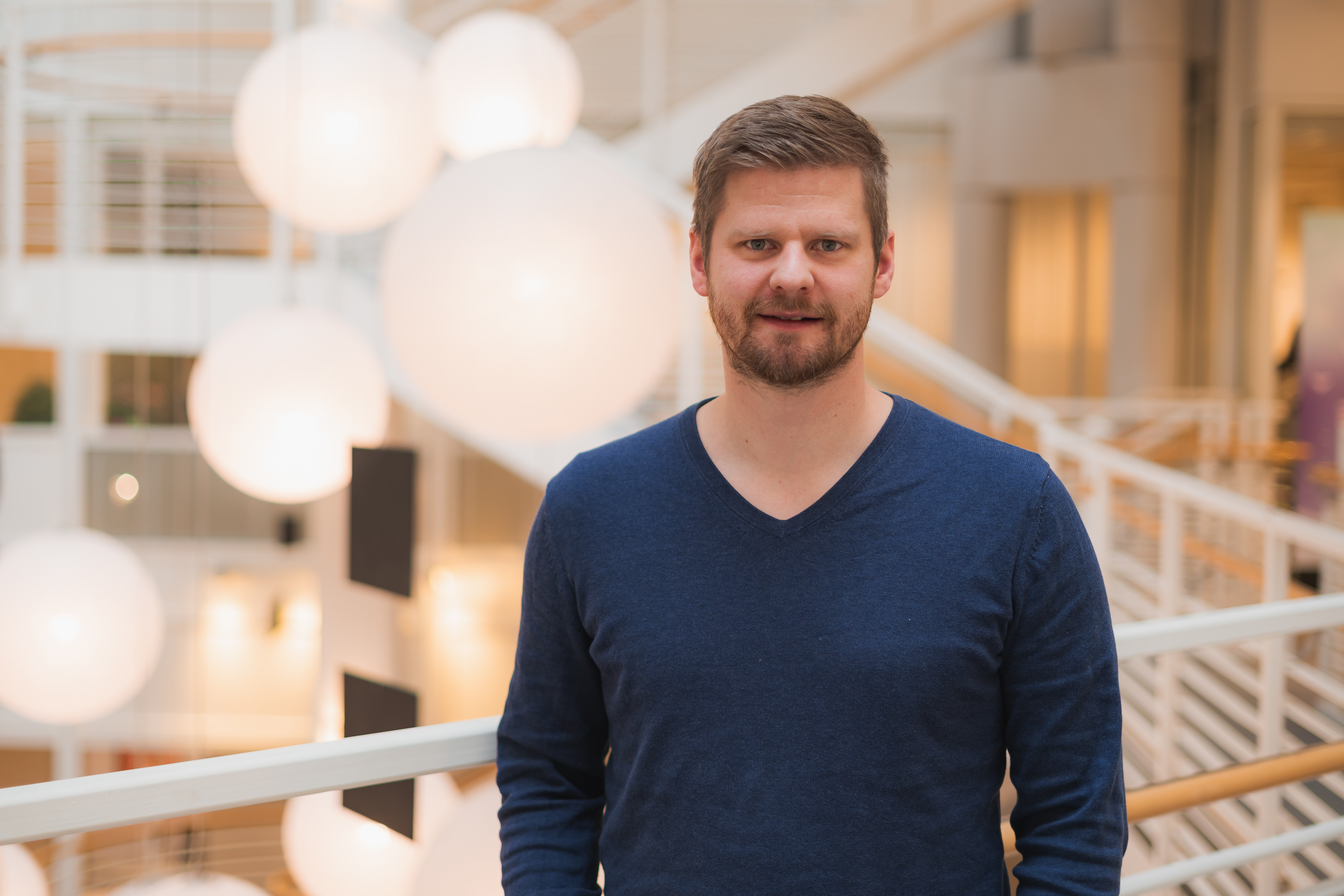 Foto av mann i blå genser foran store kulelamper.
