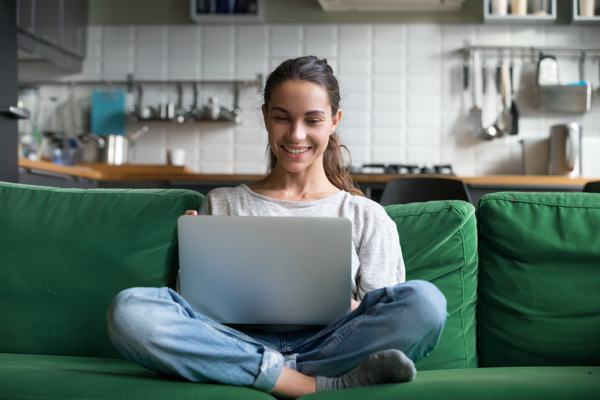 Bilde av ung kvinne som sitter i en grønn sofa med laptop på fanget.