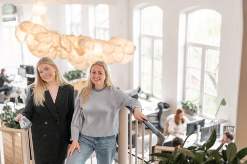 To personer står i en trapp i et lyst kontorlokale med arbeidsplasser i bakgrunnen.