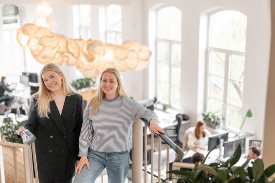 To personer står i en trapp i et lyst kontorlokale med arbeidsplasser i bakgrunnen.