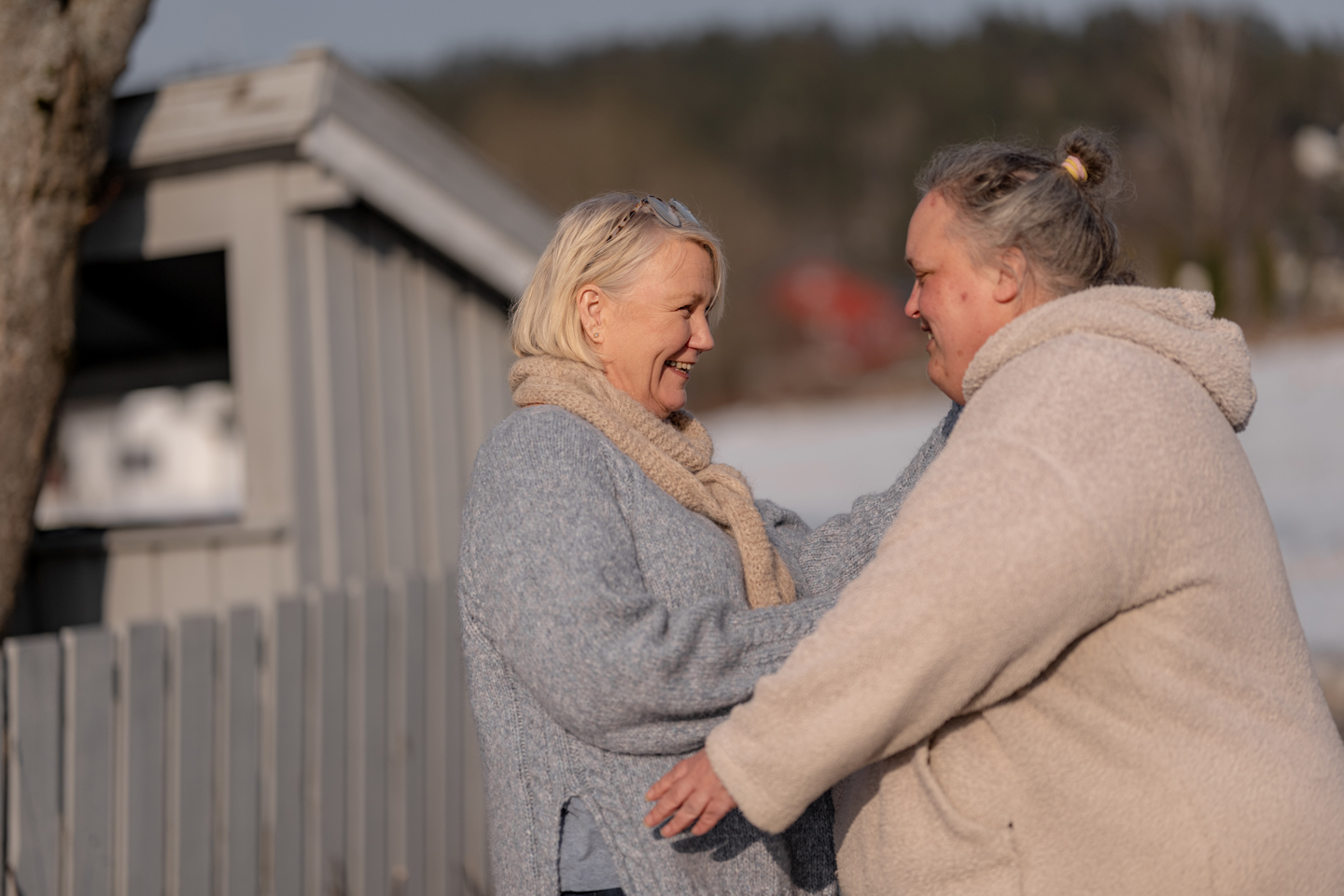 To personer står ute og snakker sammen ved et gjerde en vinterdag