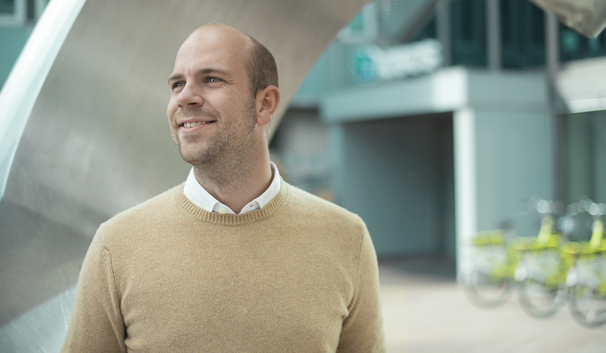 Andreas Hansen fra OBOS står foran en skulptur i aluminium. Han har på seg hvit skjorte under en beige genser, ser mot venstre og smiler.