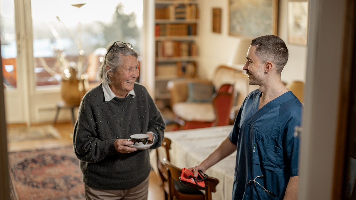 Helsefagarbeider som hjelper og smiler til en eldre person i en bolig