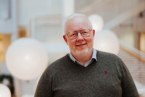 Portrett av Anders som står på campus med trapper i bakgrunnen. 