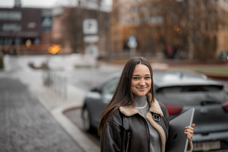 Student står utendørs på en parkeringsplass og holder en bærbar datamaskin.