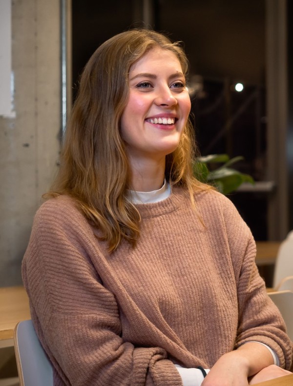 Bilde av Sophia Aronsen som sitter ved et bord i en kantine og smiler bredt.