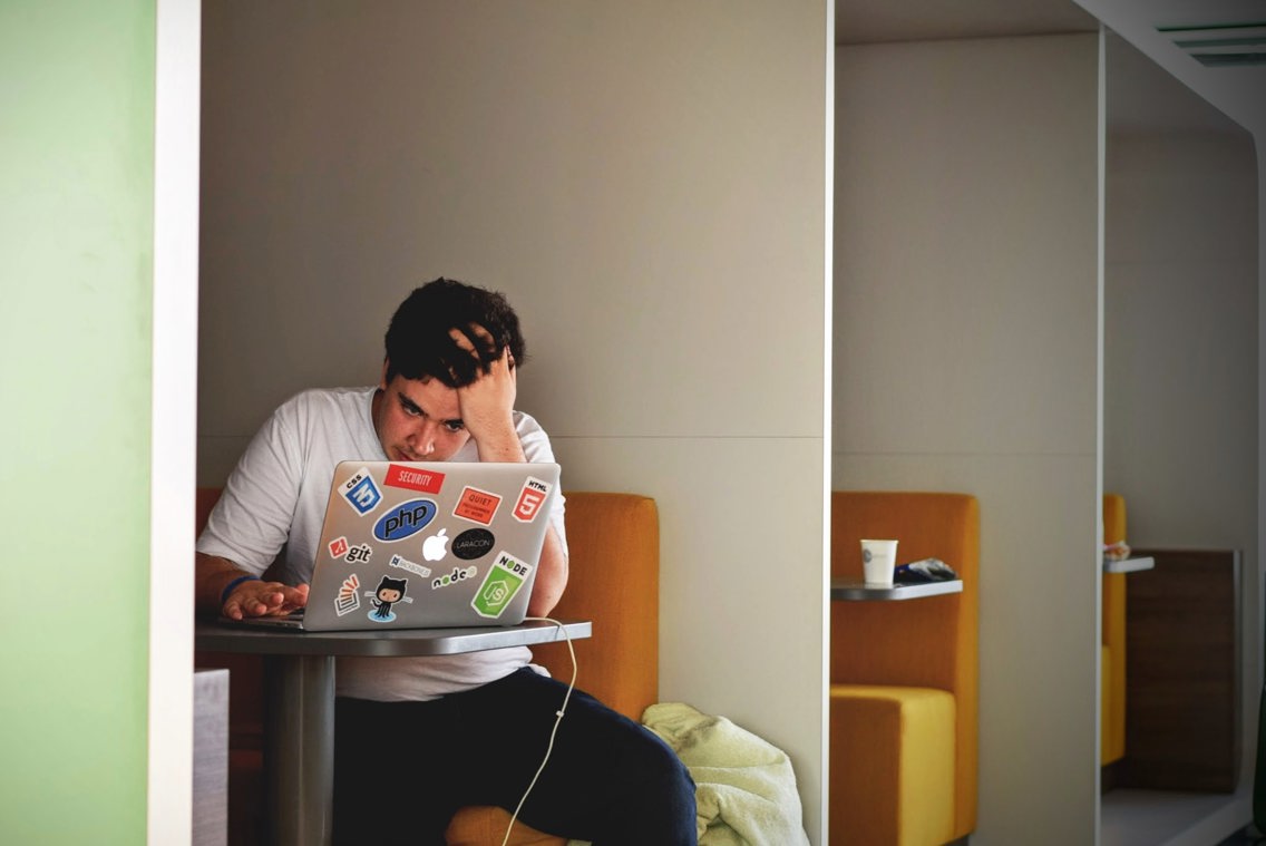 Ung mann tar seg til håret i frustrasjon foran laptop.