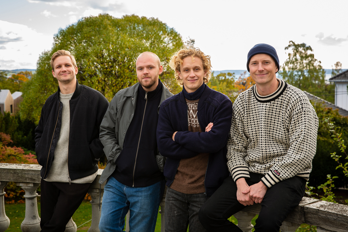 Foto av fire menn som lener seg til et rekkverk.