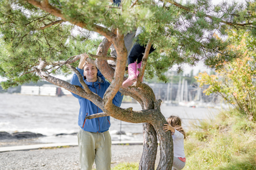 Barn leker i et tre med SFO-ansatt som smiler inn i kamera