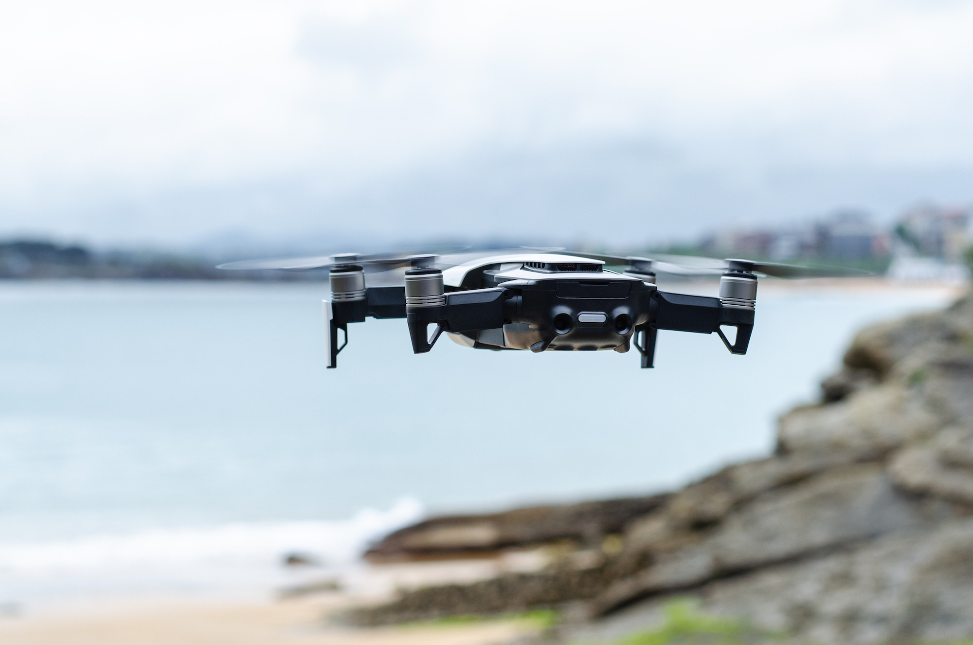 En drone flyr over et landskap med svaberg, hav og himmel i bakgrunnen.