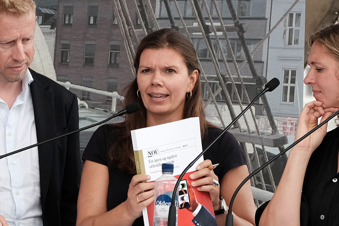 Kvinne debatterer ivrig mens hun holder opp en nytrykket rapport. 