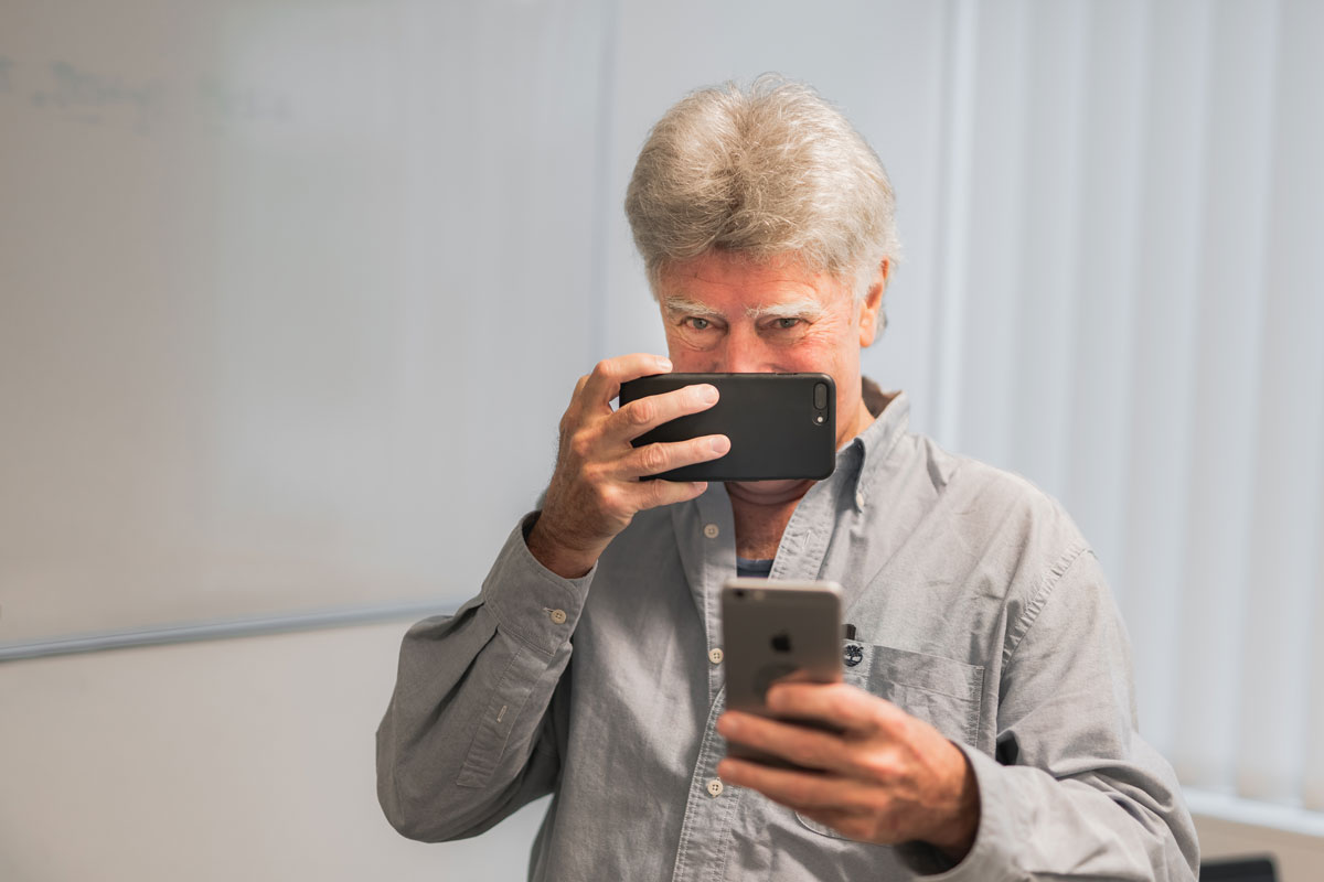 Older man holding two iPhones in front of his face and chest.