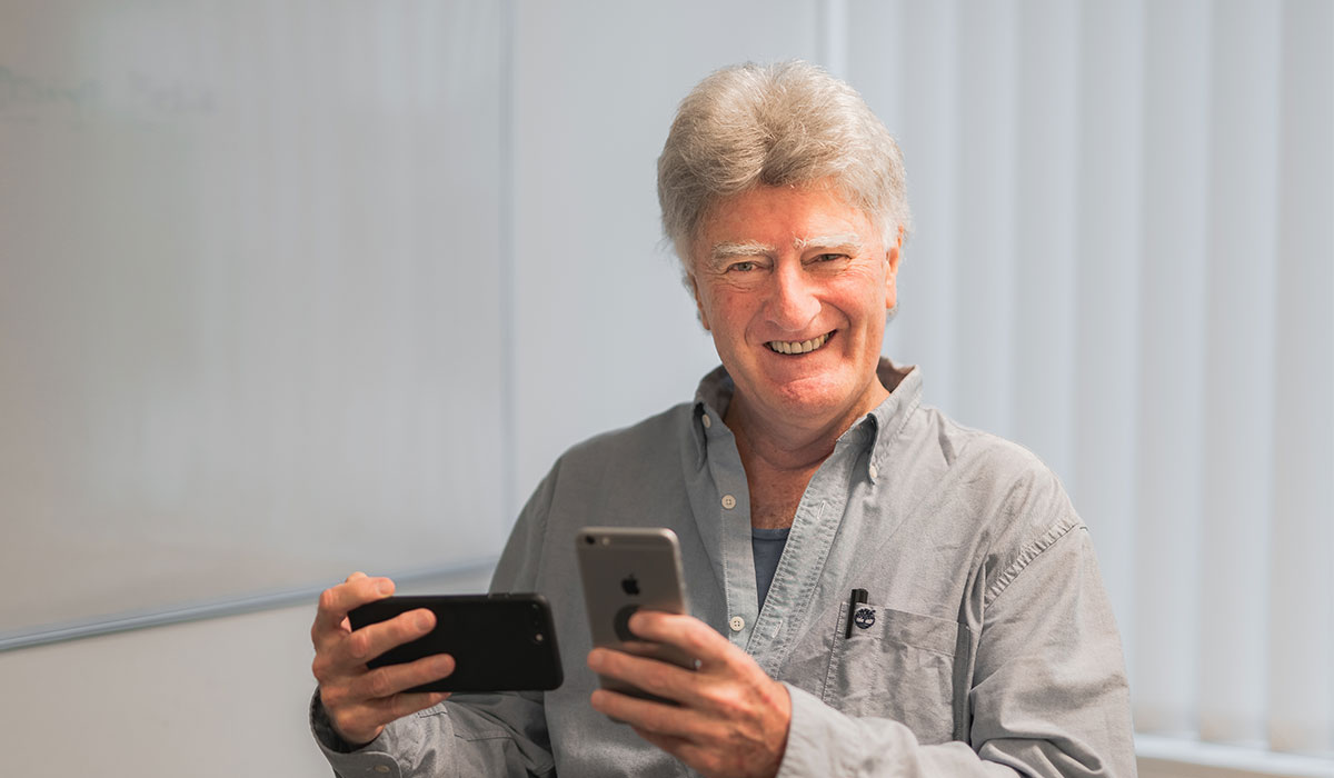 Older man holding two iPhones , one in each hand.