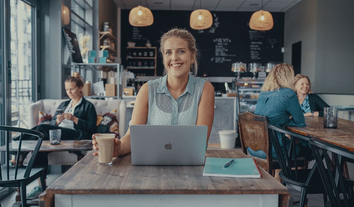 Foto av kvinne med laptop og kaffe på en kafé.