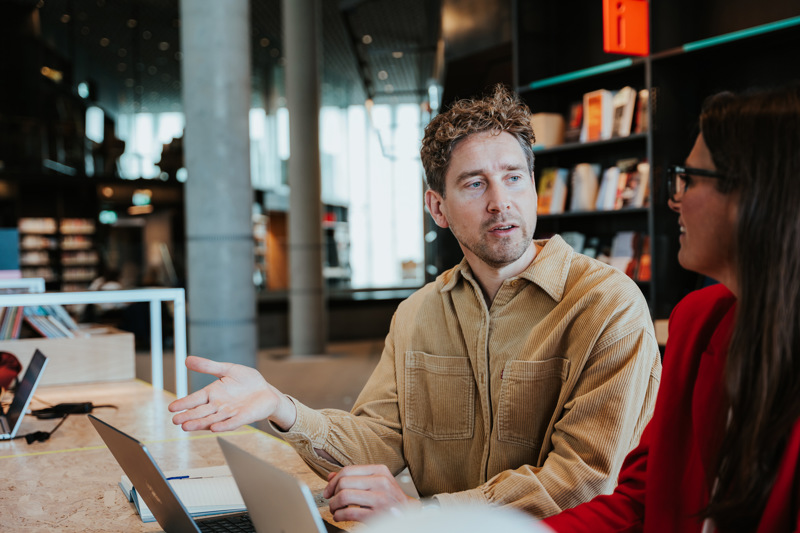 Mann og kvinne sitter og diskutere sammen på et bibliotek.