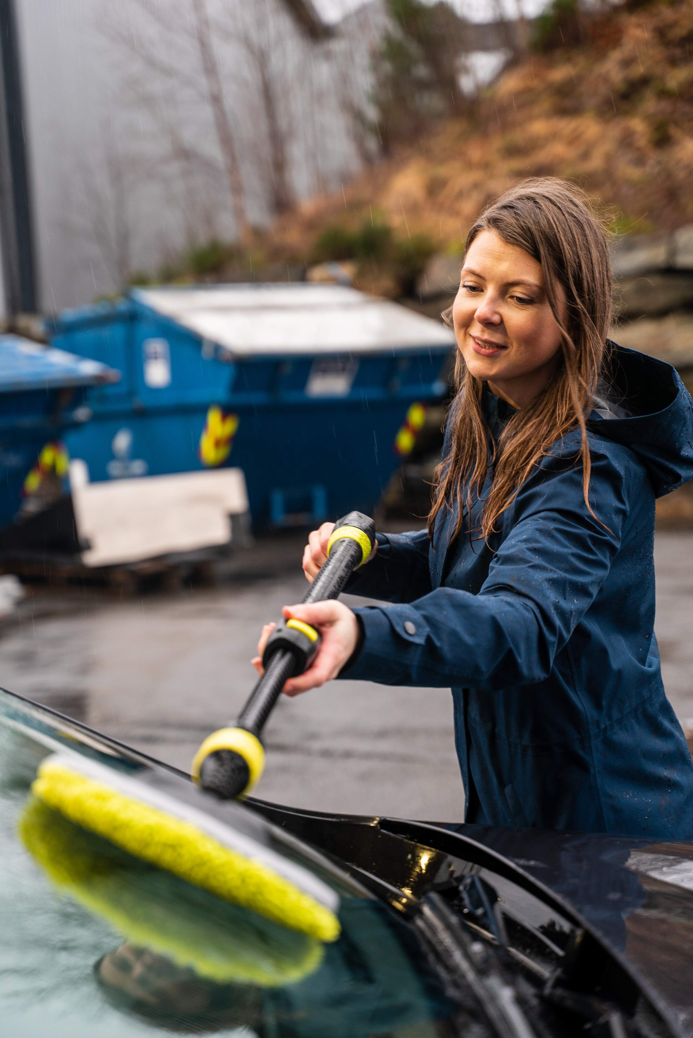 Foto av Anna som vasker frontruten på en bil ute i regnet med utstyr fra AVA of Norway. 