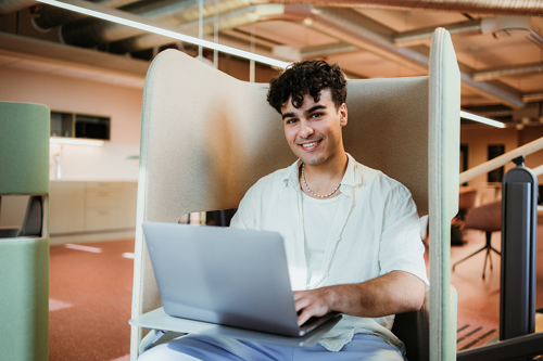 Bildelenke av ung person sittende med mac i fanget.