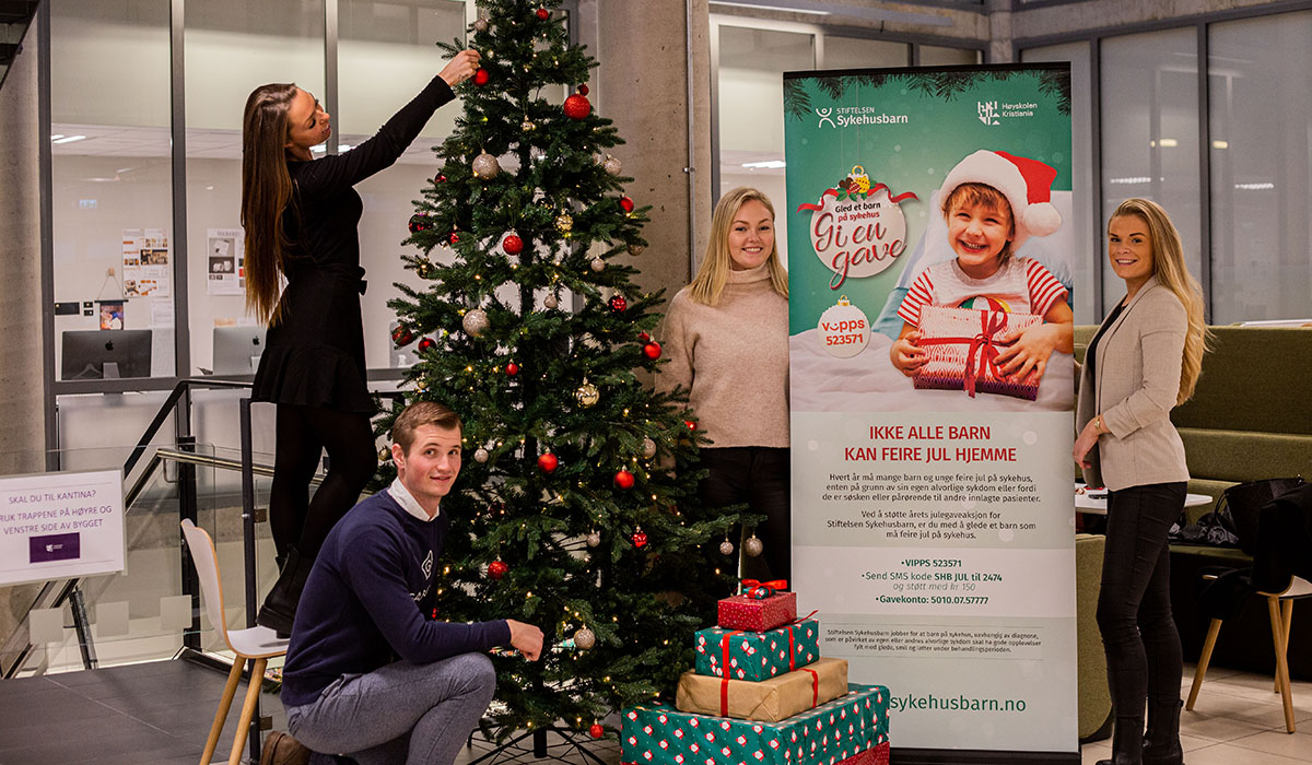 Studentene i prosjektledelse Birgit Berg, Sondre Blikberg , Ingrid Aakre, og Silje Bjerknes har laget julegaveaksjon med Stiftelsen Sykehus. Her poserer de med juletre med gaver under og en roll-up med informasjon om prosjektet.