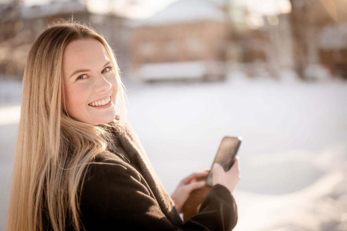 Zandra står med en mobiltelefon i et vinterlandskap og smiler til kamera.
