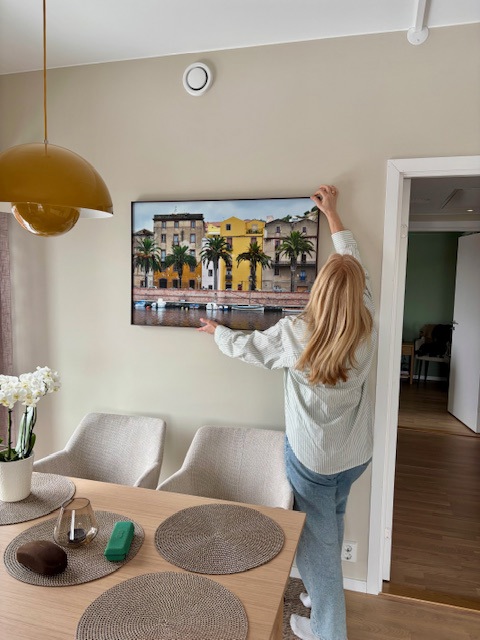 Marita henger opp et bilde i en stue