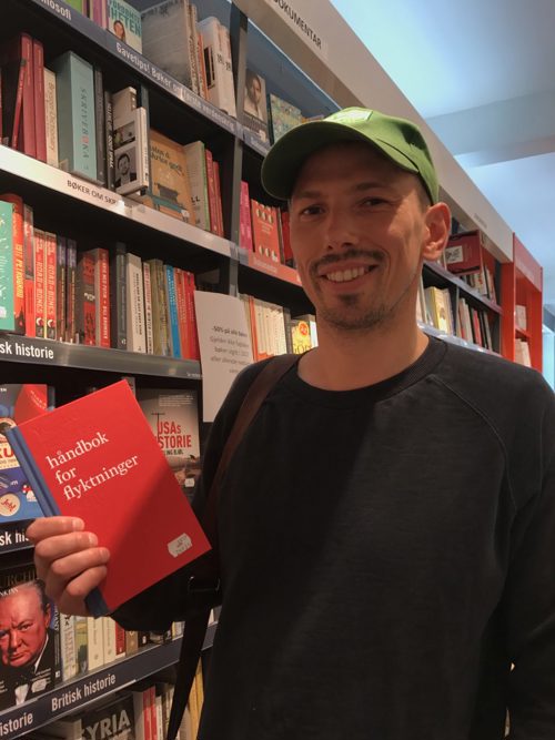 Foto av mann ved en bokhylle som viser frm en bok.