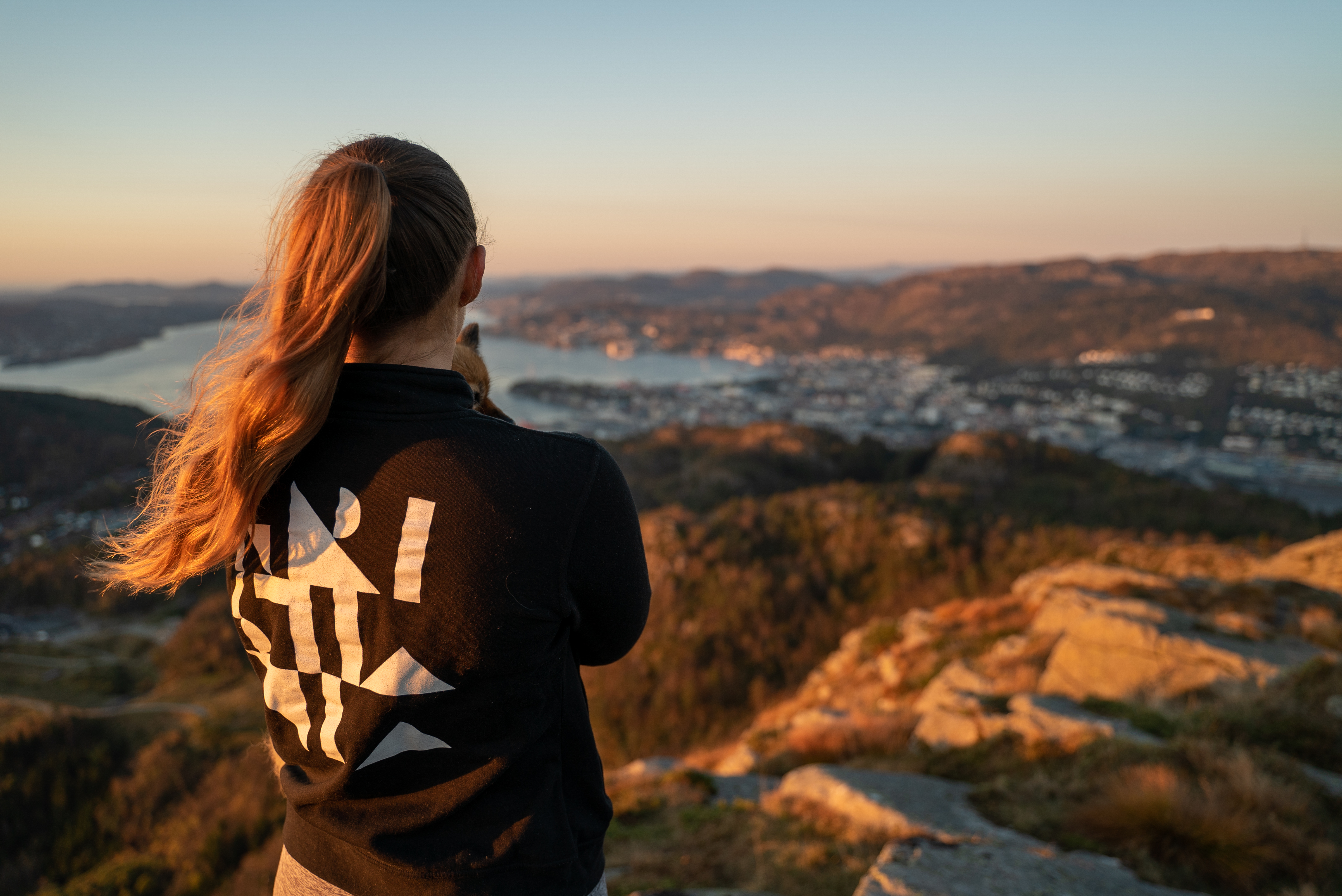 Foto av ung kvinne på toppen av Løvstakken, med ryggen til kamera og nesen vendt i retning Bergen sentrum.