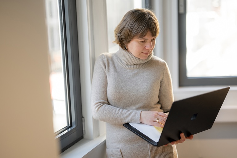 Person står ved et vindu med en bærbar PC i hendene og arbeider digitalt.