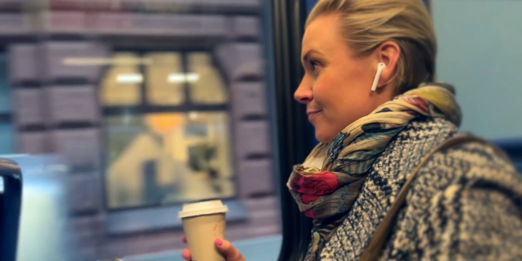 Kvinne sitter med høretelefoner og kaffekopp på bussen