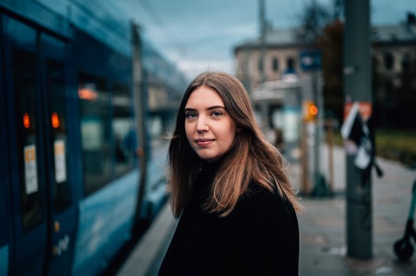 Ung student fra Høyskolen Kristiania som står ved på et trikkestopp