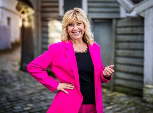 Marit Warncke i sjokkrosa drakt poserer med hånden i siden og et stort smil