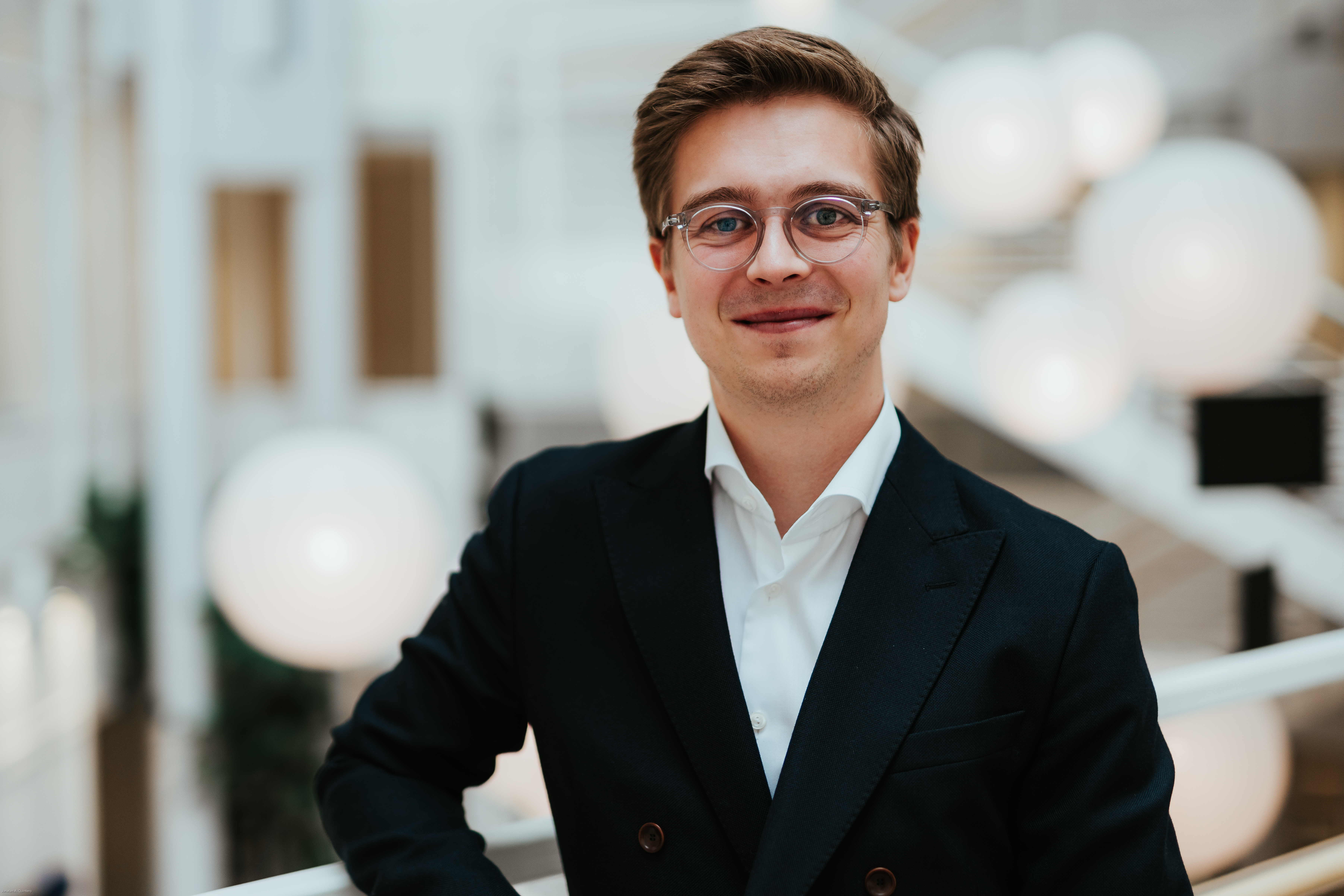 Foto av mann med briller ikledd hvit skjorte og blazer som støtter seg på et rekkverk.