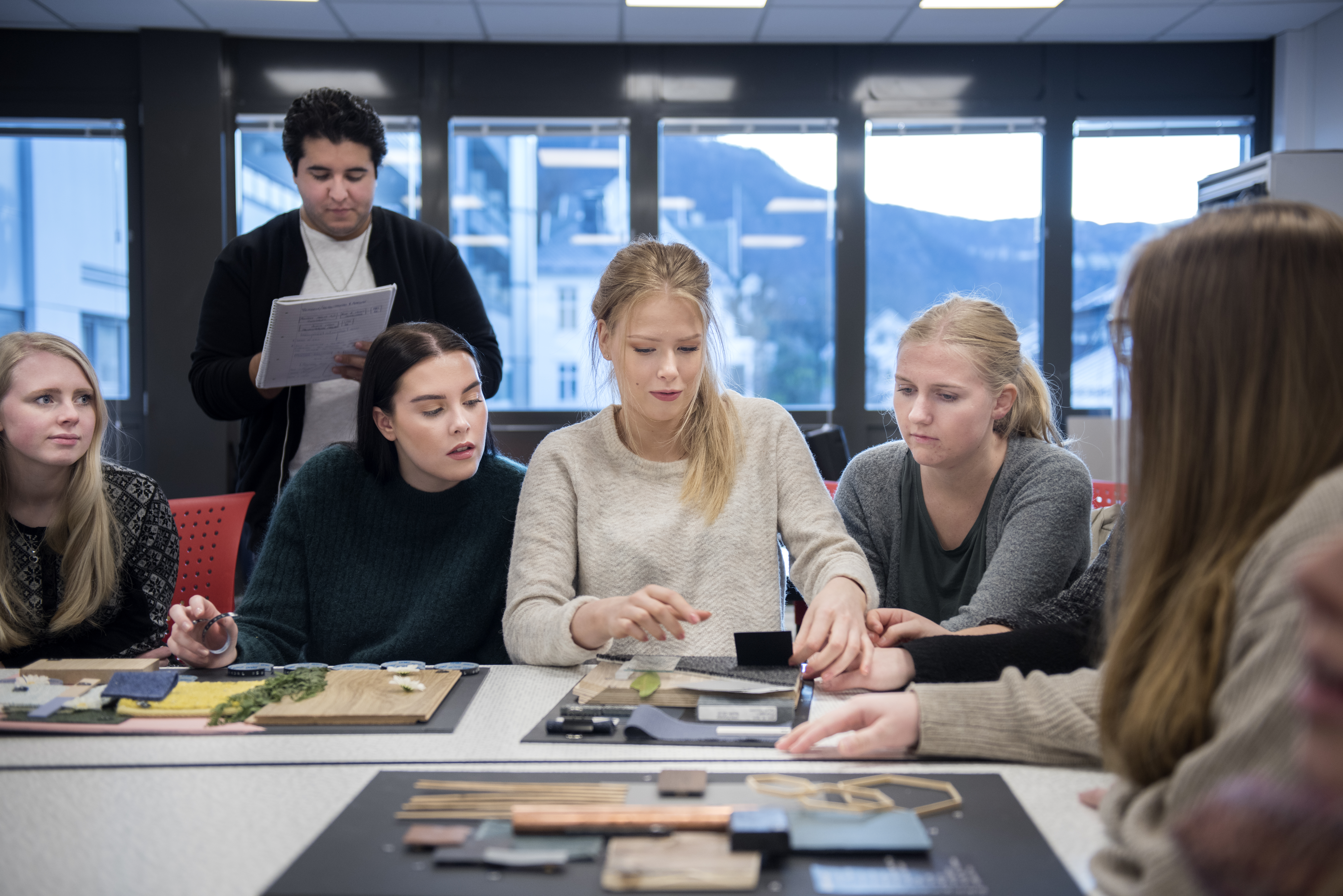 Foto av fem kvinnelige og en mannlig student som jobber med en praktisk oppgave i et klasserom.