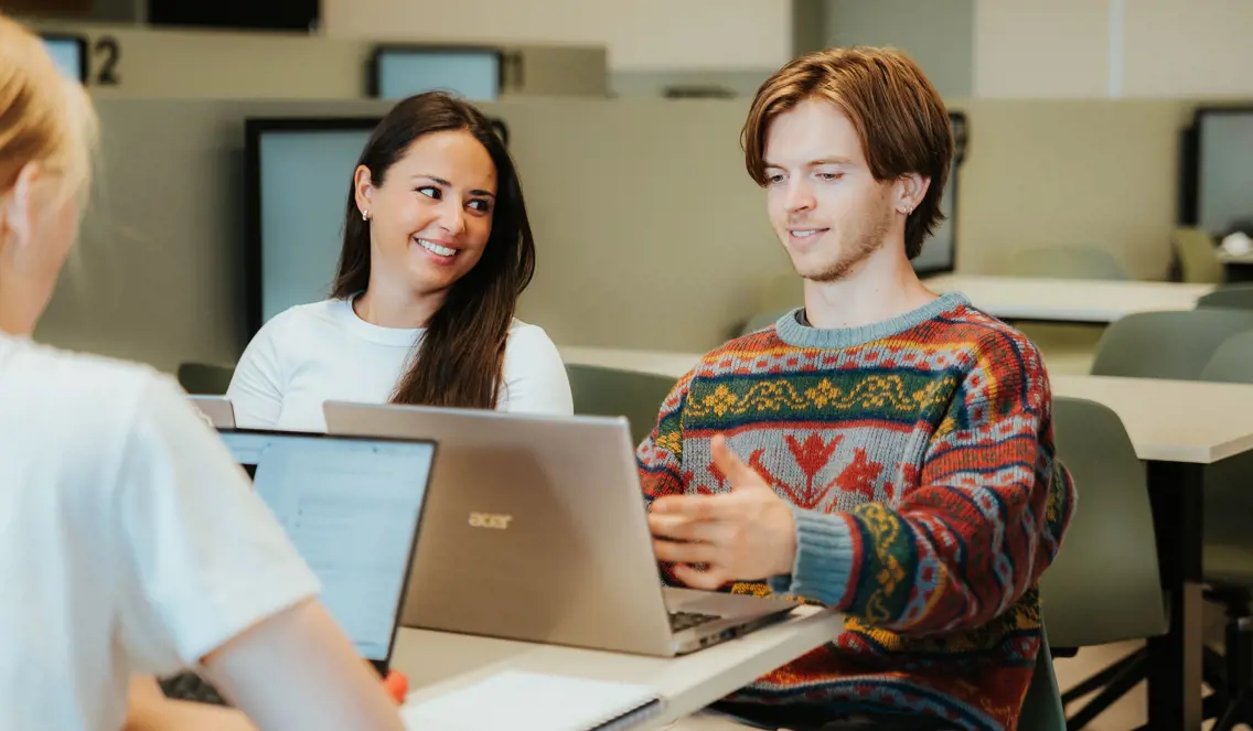 Tre studenter sitter rundt en pult med PC'ene sine og jobber sammen