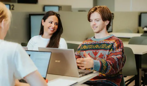 Tre studenter sitter rundt en pult med PC'ene sine og jobber sammen