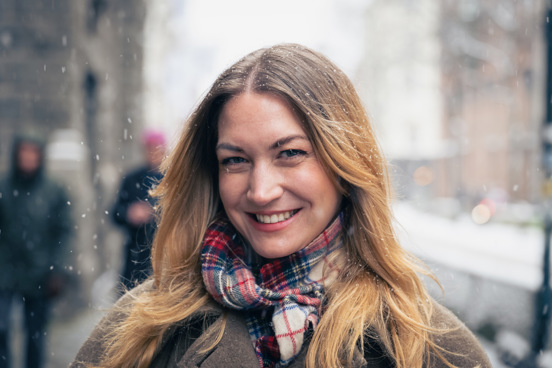 Portrett av Mina som står ute og smiler til kamera, mens snøen daler ned rundt henne. 