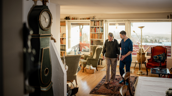 En person støtter en annen mens de går gjennom en stue i et hjemmemiljø