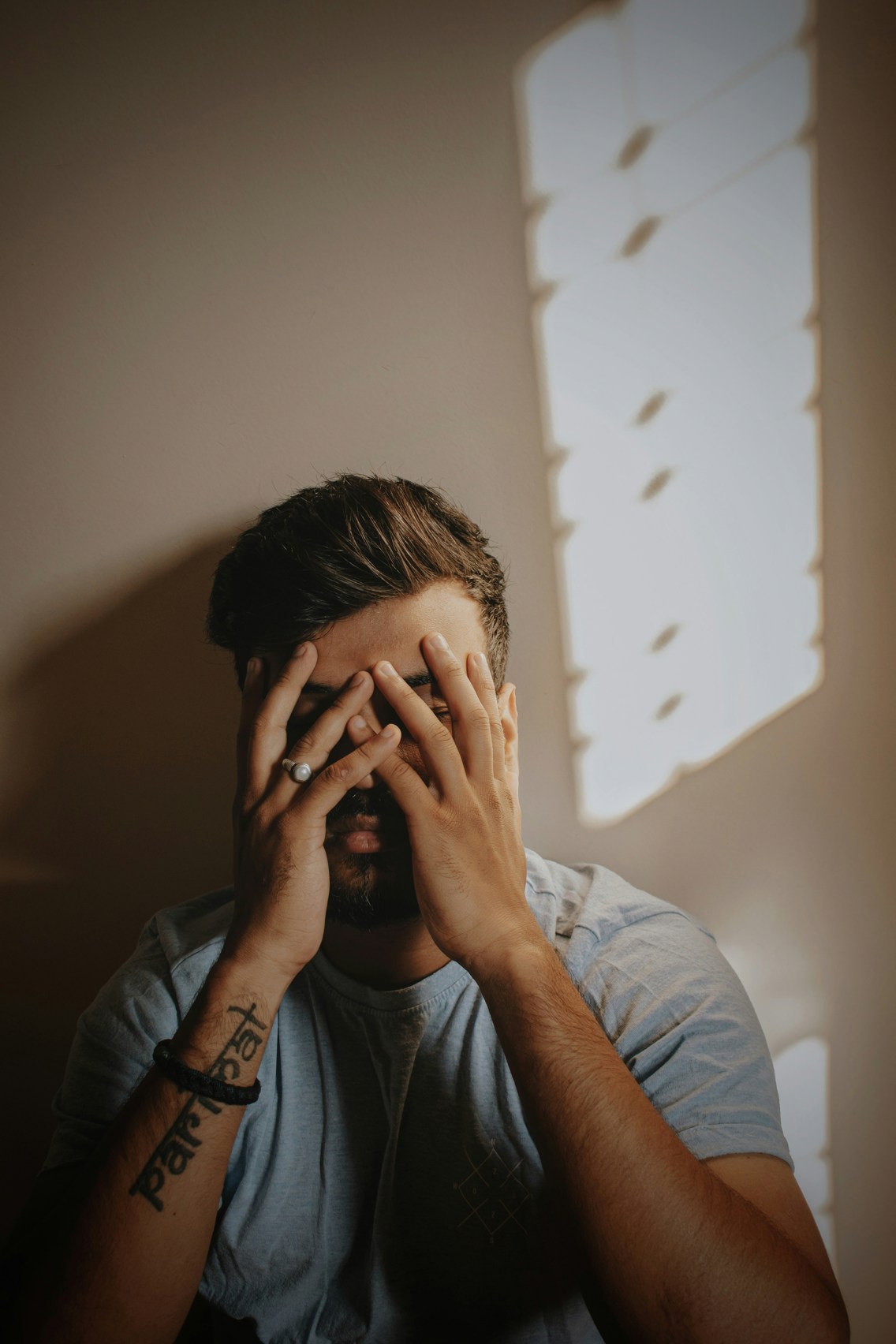 En ung mann sitter med hendene foran ansiktet sitt og ser lei seg ut