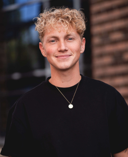 Oliver Gjølberg har en Bachelor i kreativitet, innovasjon og forretningsutvikling fra Høyskolen Kristiania. Han har blondt, krøllete hår og en svart genser på seg.