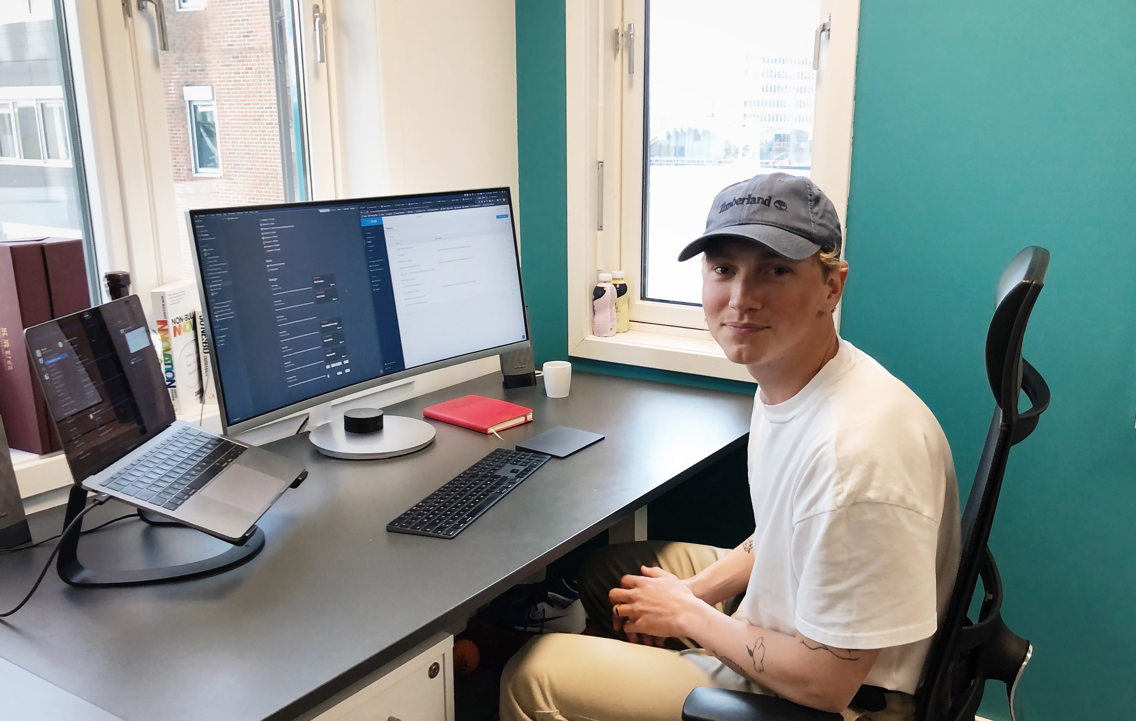 Foto av Oliver foran pc'en på kontorplassen sin.