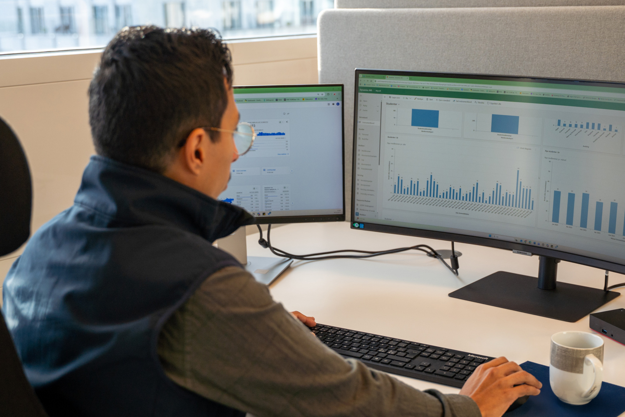 Luis sitter på kontoret med ryggen til kamera, foran to skjermer som viser ulike grafer.