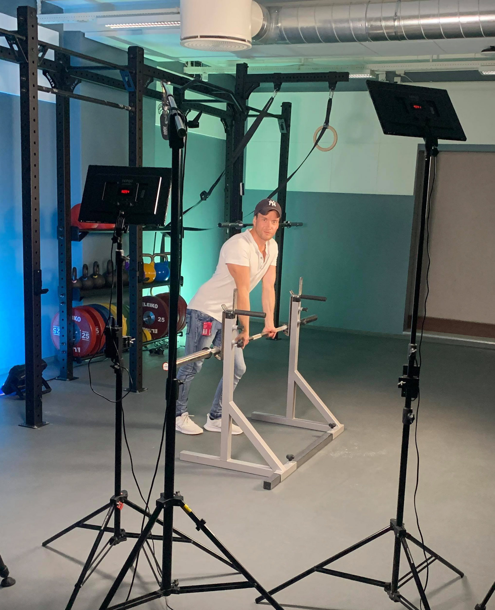 Micheal står ved en «rack» i et treningsstudio med filmutstyr er rigget rundt han.
