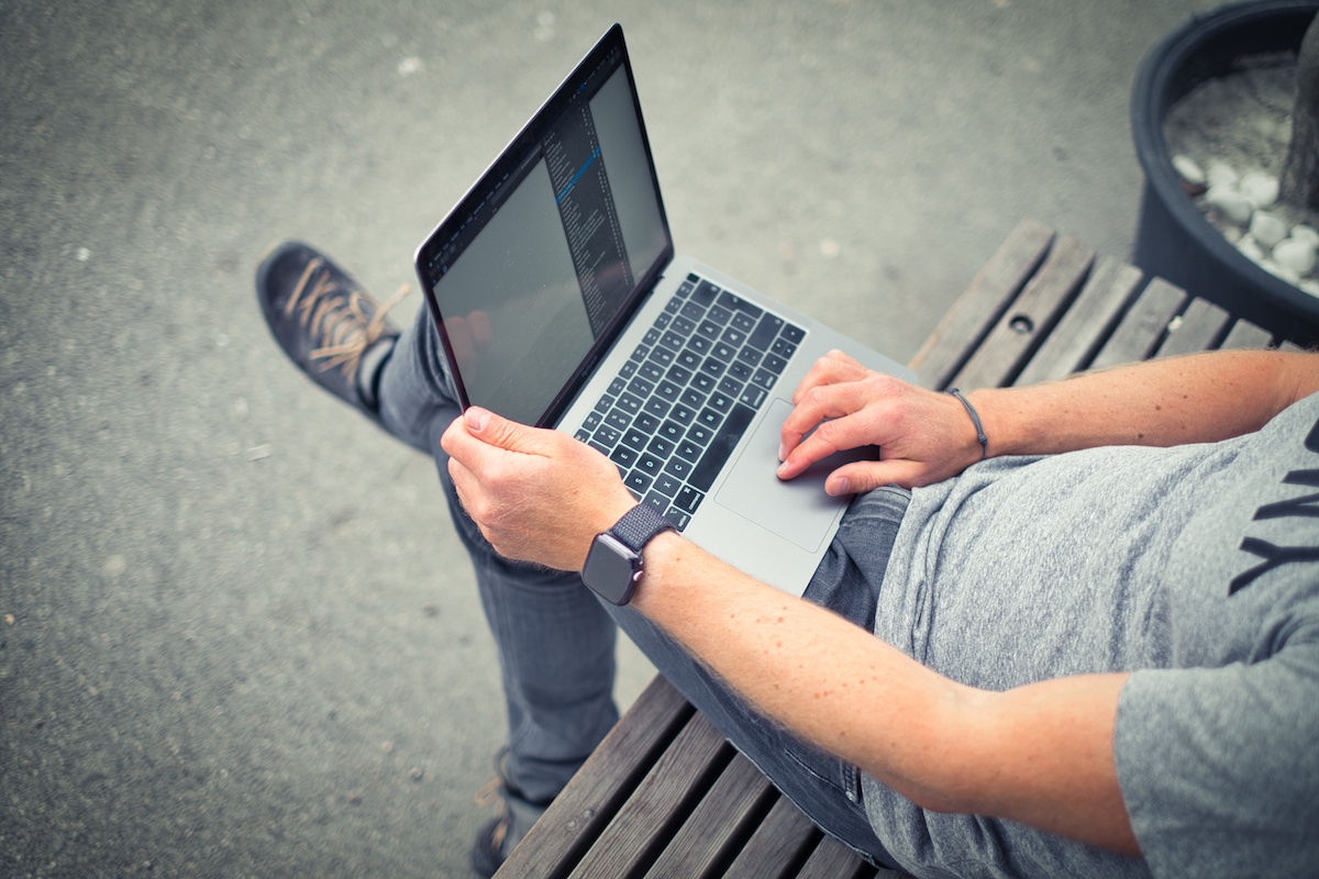 Detaljfoto av mann på benk som jobber med en laptop.