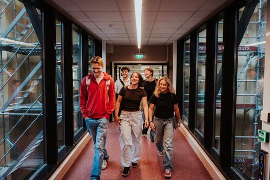 Fem studenter går i en gang med glassvegger på begge sider.