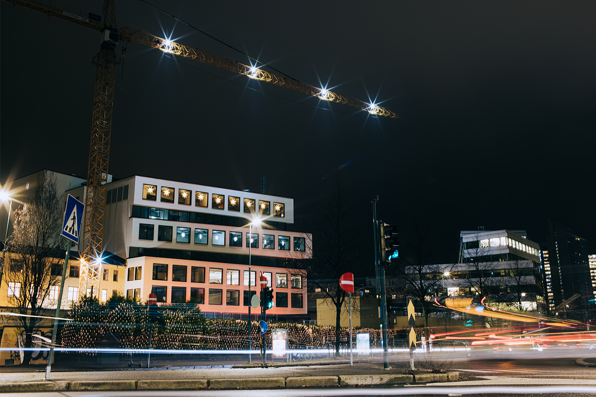 Bygg og byggeplass i mørket med heisekran utenfor.