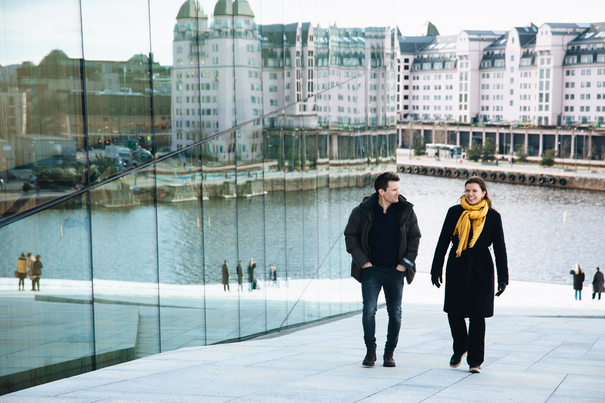 Foto av mann og kvinne som går på operataket i Oslo, med havnen i bakgrunnen.