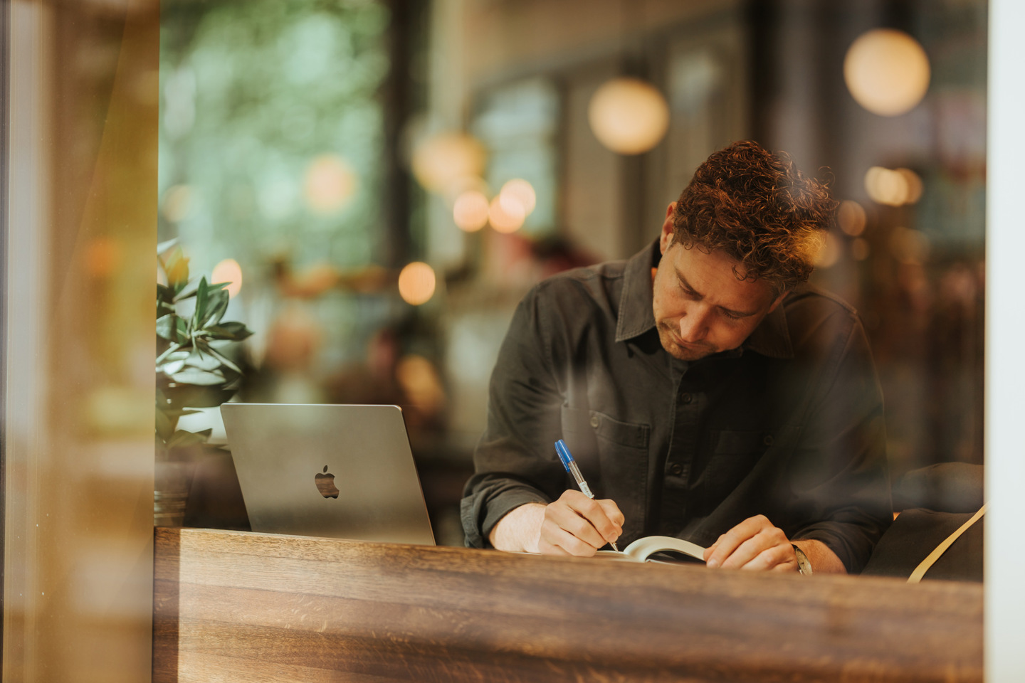 Person jobber med bok og mac på kafé.