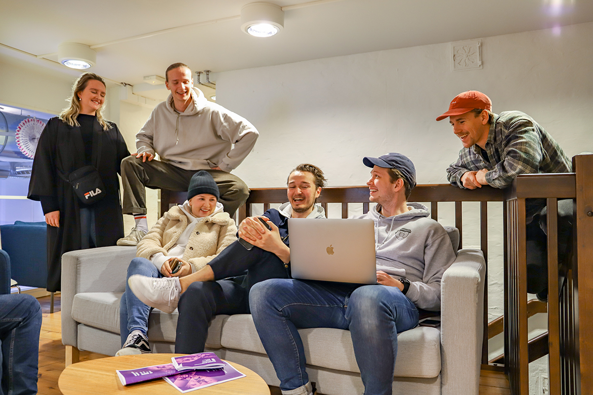 Filmstudenter på skolebygg Vågen i Bergen sitter i og rundt en sofa og ser på en Mac
