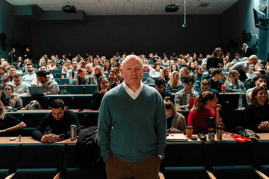 Foto av Nikolai Tangen foran auditorium fylt av studenter.